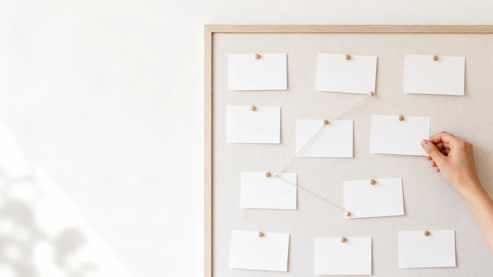 A hand pinning a blank card onto a board of index cards linked by thread.