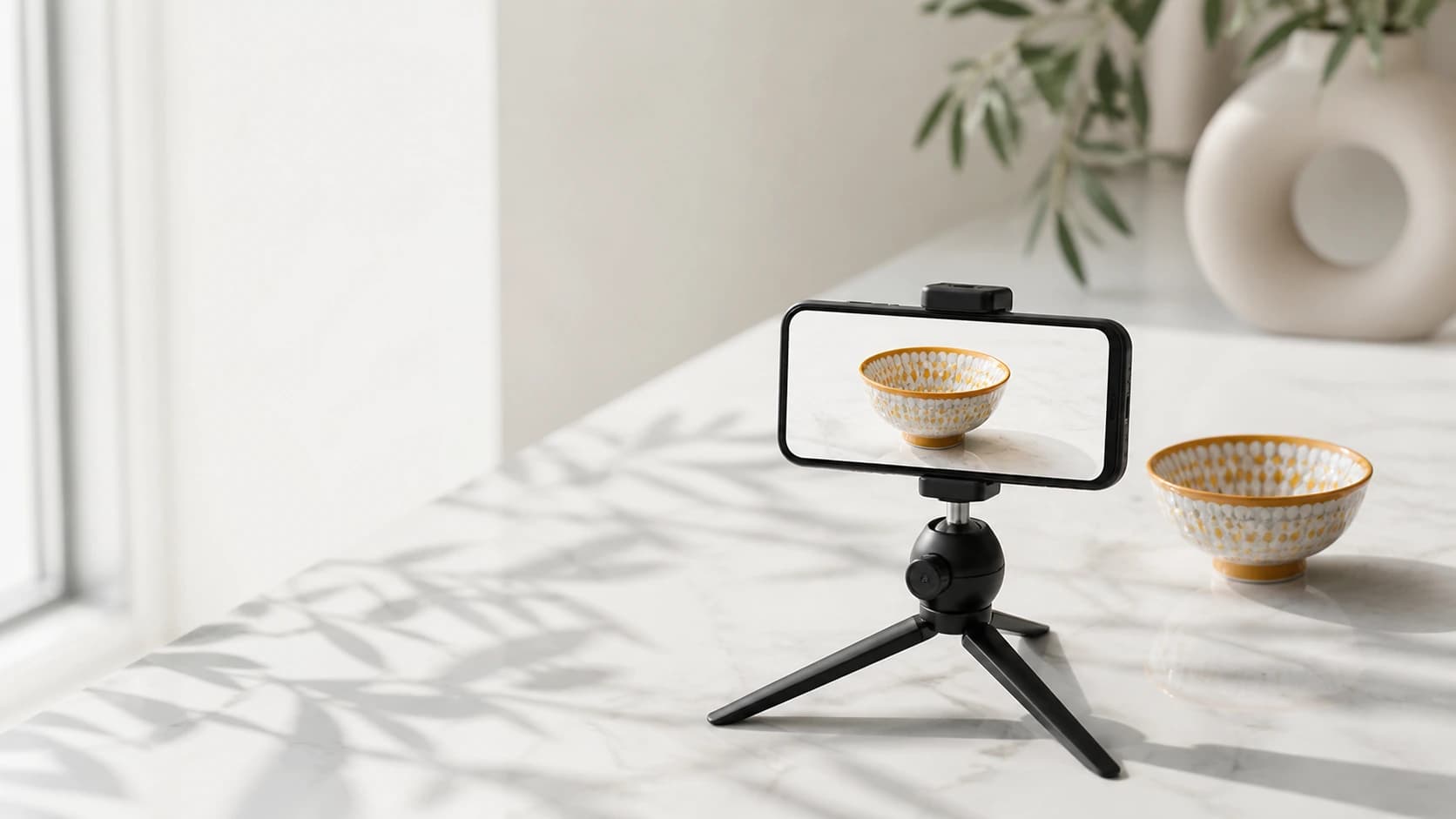 A phone on a small tripod filming a Moroccan ceramic bowl on a marble surface.